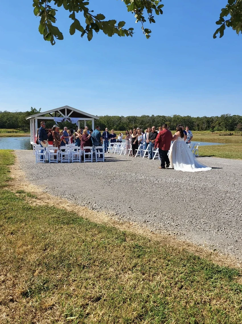 Cole and Emily walking from their lakeside ceremony as standing guests watch beside the pavilion in Normangee, Texas