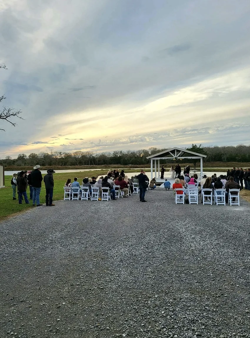 Wide view of guests seated on the ceremony lawn facing the lakeside pavilion at a Texas wedding venue near Bryan and College Station