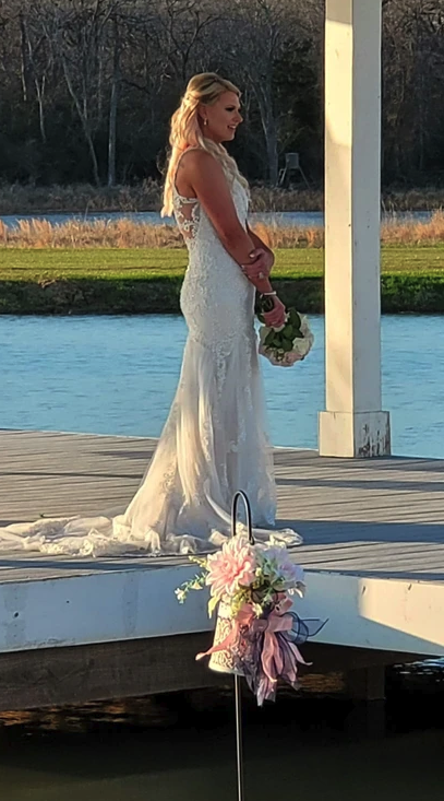 Bride in lace gown standing on the lakeside dock holding her bouquet at golden hour