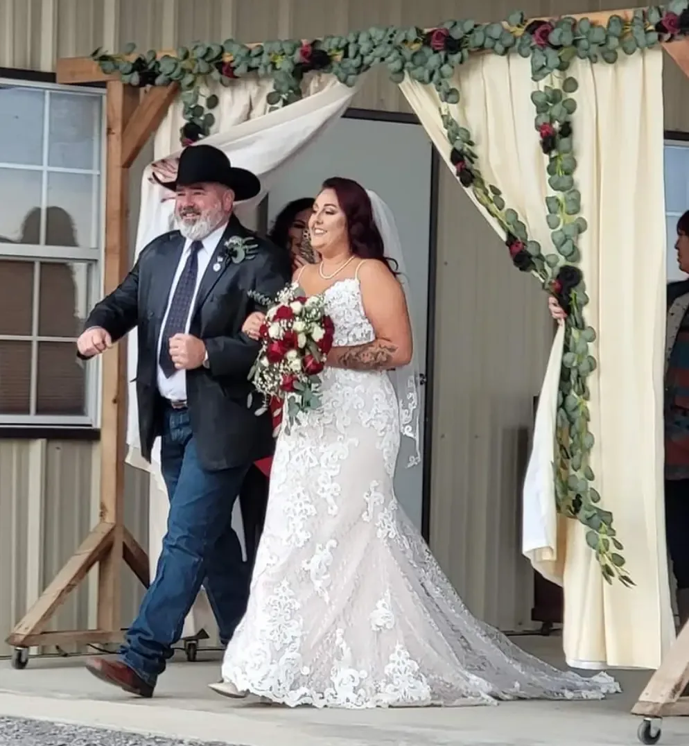 Bride escorted down the aisle through a draped entrance and floral arch at Reverie at Diamond D wedding venue in Normangee TX