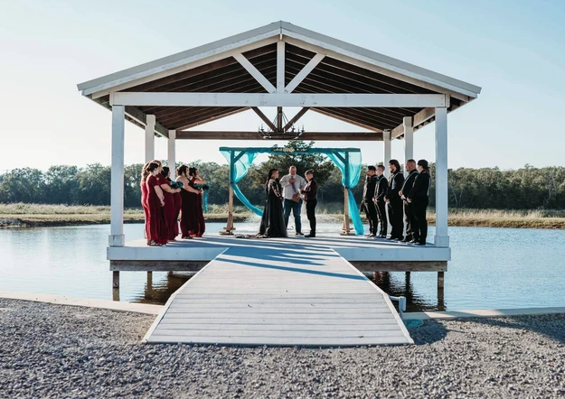 Symmetrical view of the vows on the lakeside dock with the wedding party flanking the couple