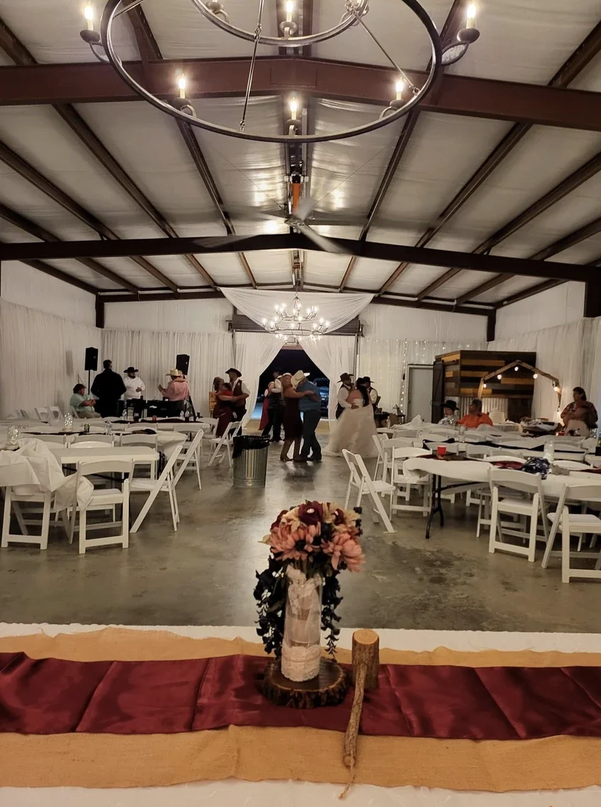 Couples dancing in the reception hall at night with a burgundy runner and floral centerpiece in the foreground