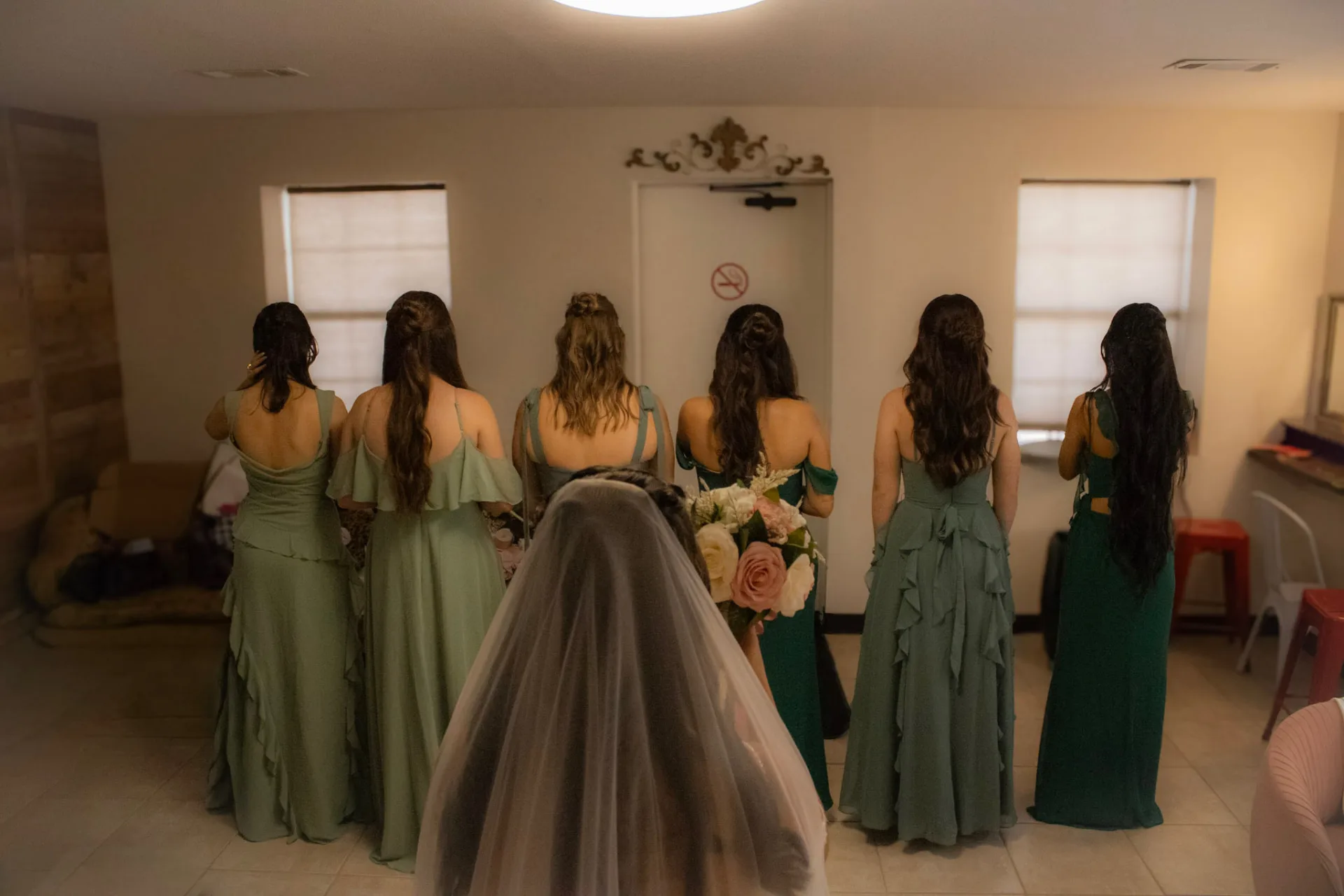Bridesmaids in sage and emerald gowns turning for a first look with the bride in the bridal suite