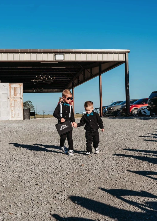 Two young ring bearers in black suits carrying a Ring Security briefcase across the gravel