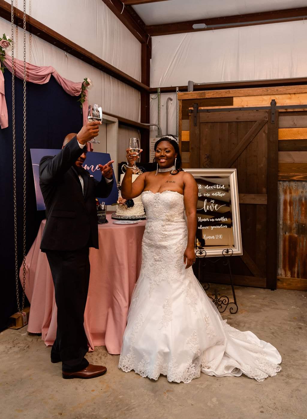 Bride and groom raising a champagne toast beside their blush-draped cake table