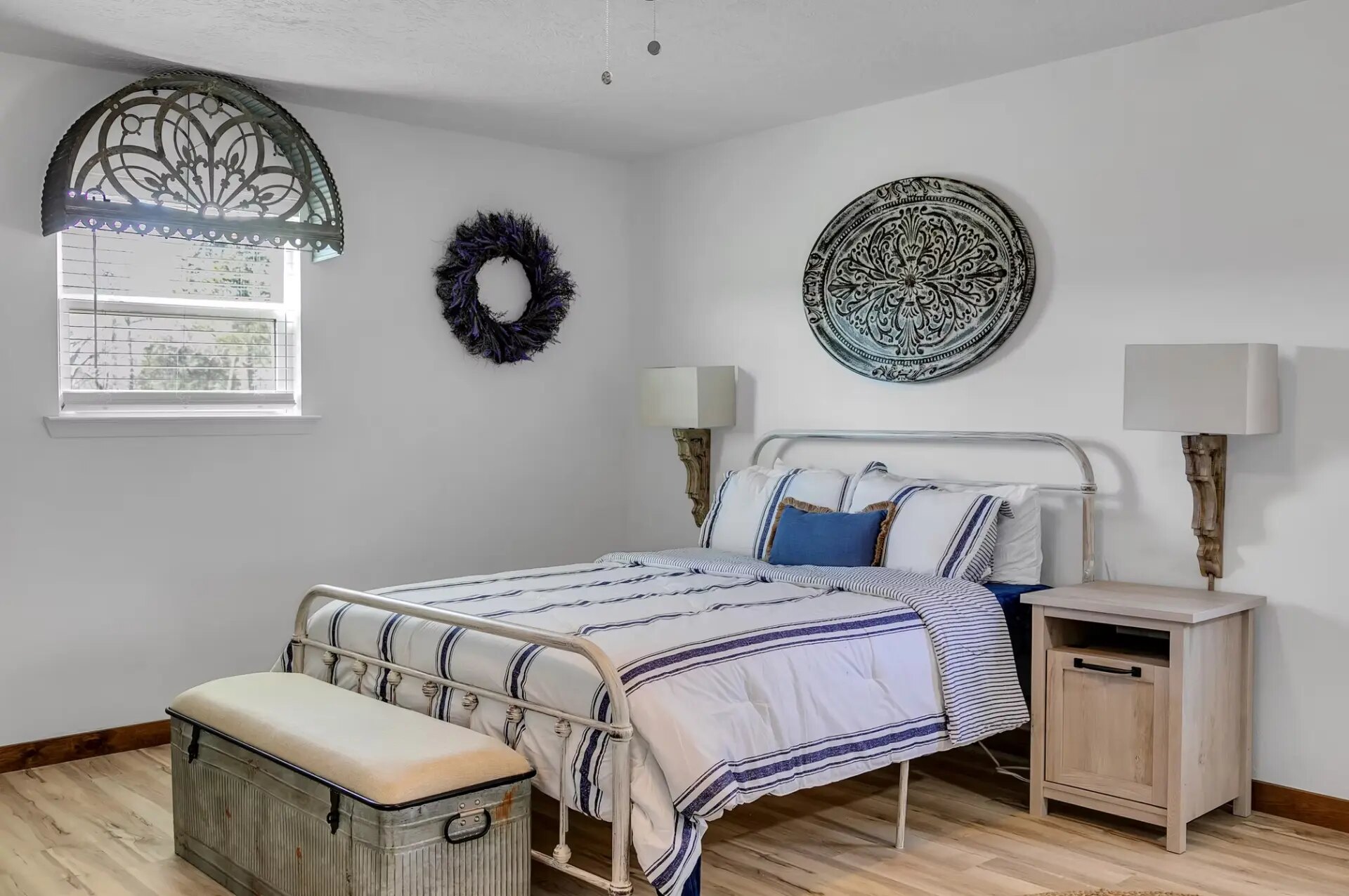 Farmhouse bedroom with a white iron bed, striped linens and vintage trunk bench at Reverie at Diamond D