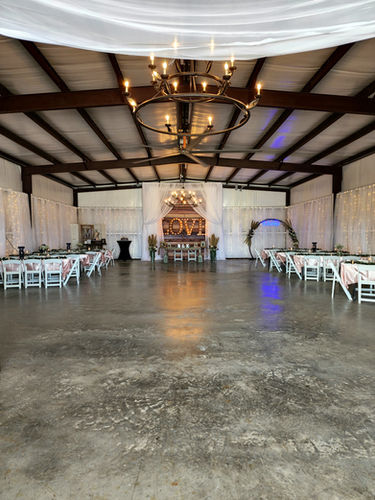 Barn interior with iron chandeliers, draped walls and long banquet tables set for a reception