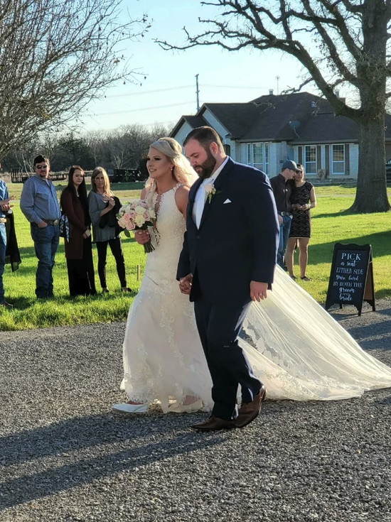 Bride and groom walking hand in hand toward the farmhouse as guests look on