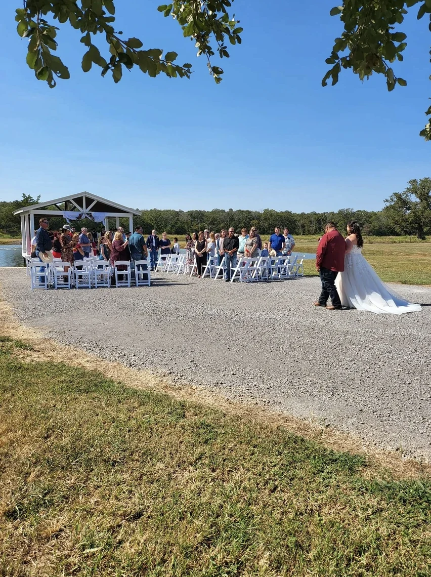 Cole and Emily walking together from the lakeside pavilion after their outdoor wedding ceremony in Normangee TX