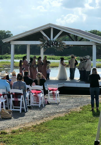 Couple exchanging vows under the lakeside pavilion with bridal party looking on