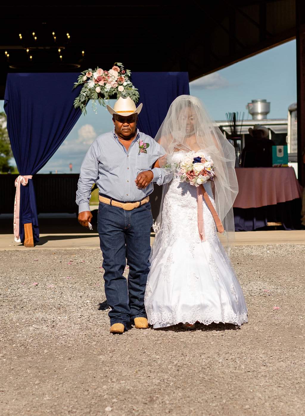 Bride escorted by her father beneath a navy draped floral arch at the barn
