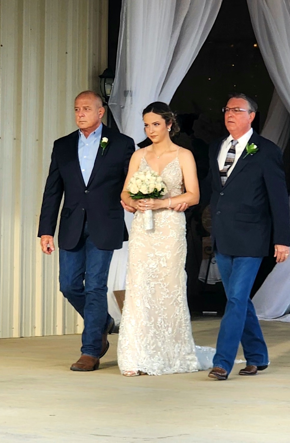 Bride escorted out of the barn by her fathers beneath white drapery before the ceremony