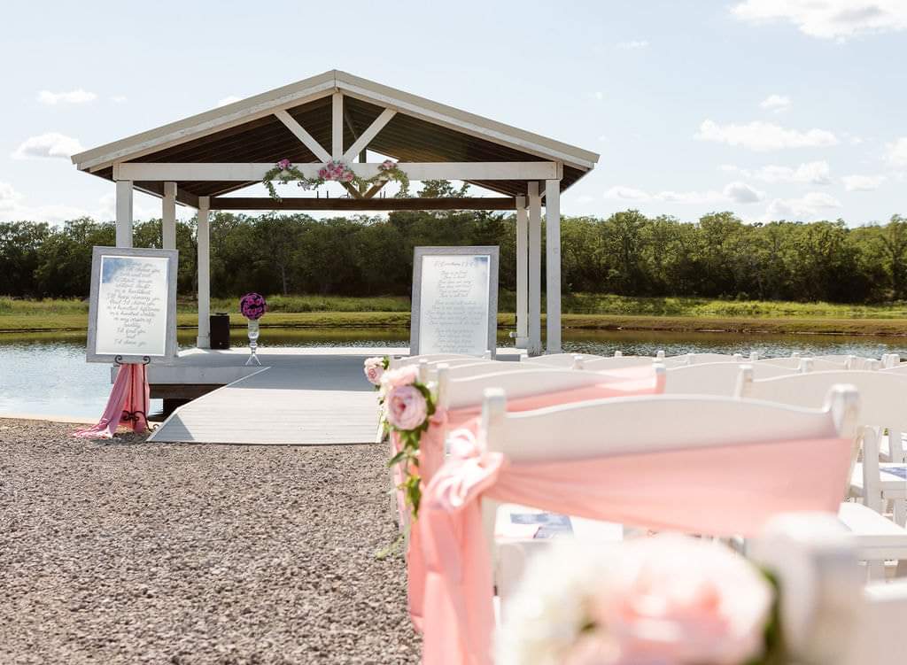 Lakeside pavilion draped in florals with framed vow signs at the aisle entrance