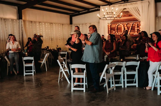 Guests standing for a toast beside twinkle-light draping and the lighted LOVE marquee