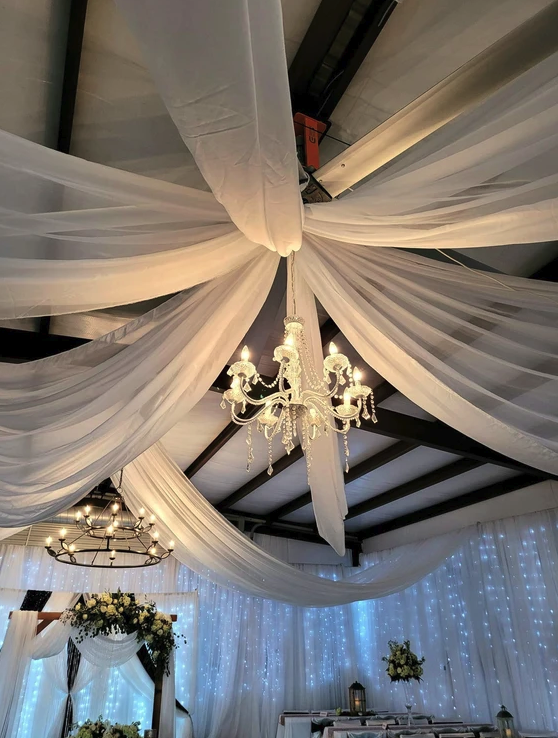 Sweeping white ceiling draping and dual chandeliers inside the reception barn
