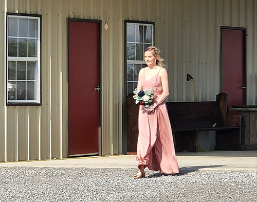Bridesmaid in blush walking past the barn's antique pews at Reverie at Diamond D