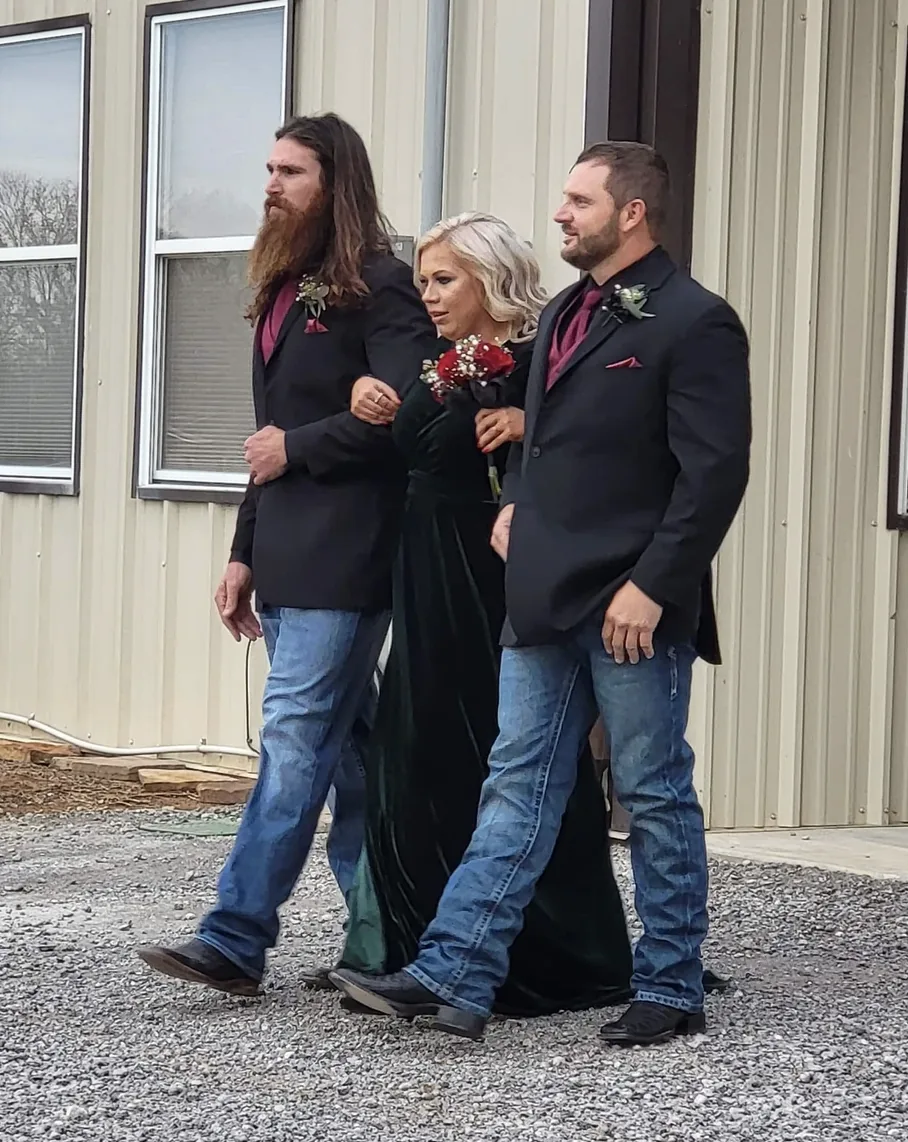 Groomsman in a black suit walking a bridesmaid in a green velvet gown during the processional at a Texas country wedding venue