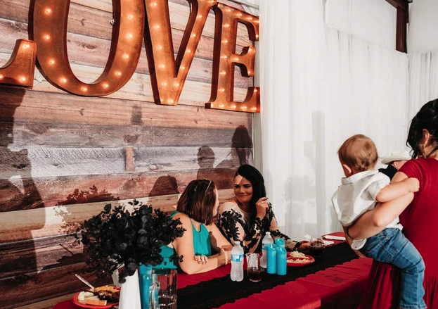 Head table beneath the lighted LOVE marquee sign with black florals and red linens