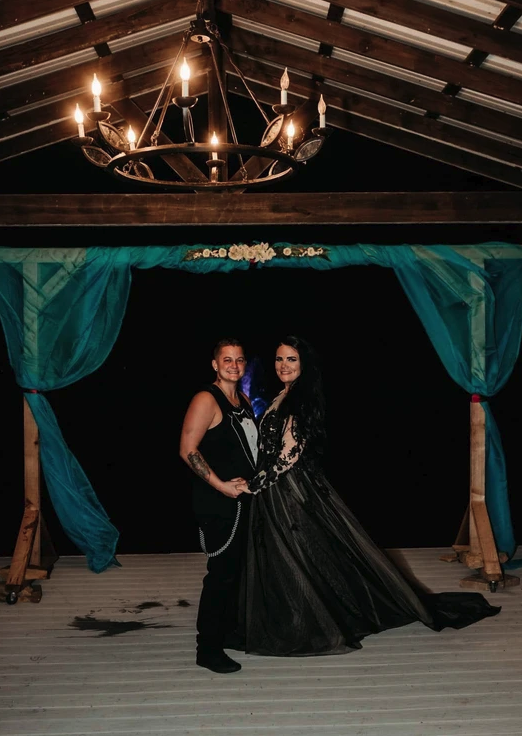Newlyweds posing under the chandelier and teal draped arbor at the lakeside pavilion after dark