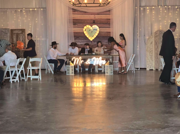 Wedding party seated at the head table with a Mr & Mrs marquee sign in the draped barn at Reverie at Diamond D