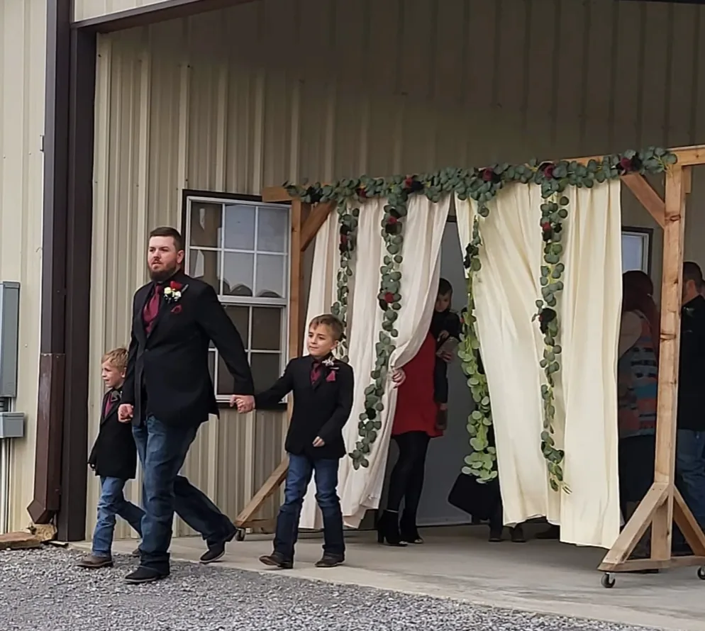 Groom walking down the ceremony aisle holding hands with two young ring bearers at Reverie at Diamond D in Normangee, Texas