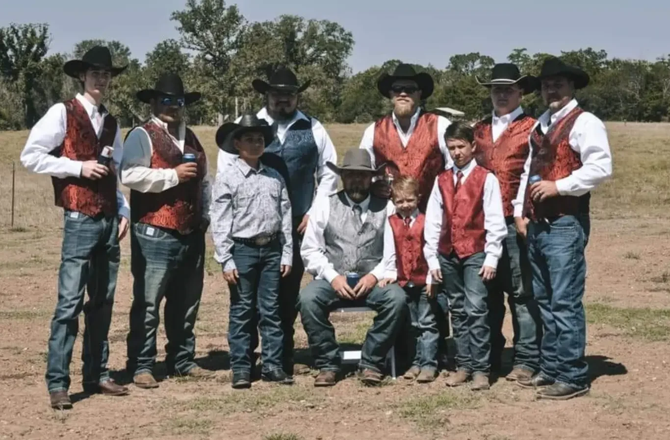 Groom and groomsmen in red vests and cowboy hats posing together in an open ranch field at a Texas wedding venue