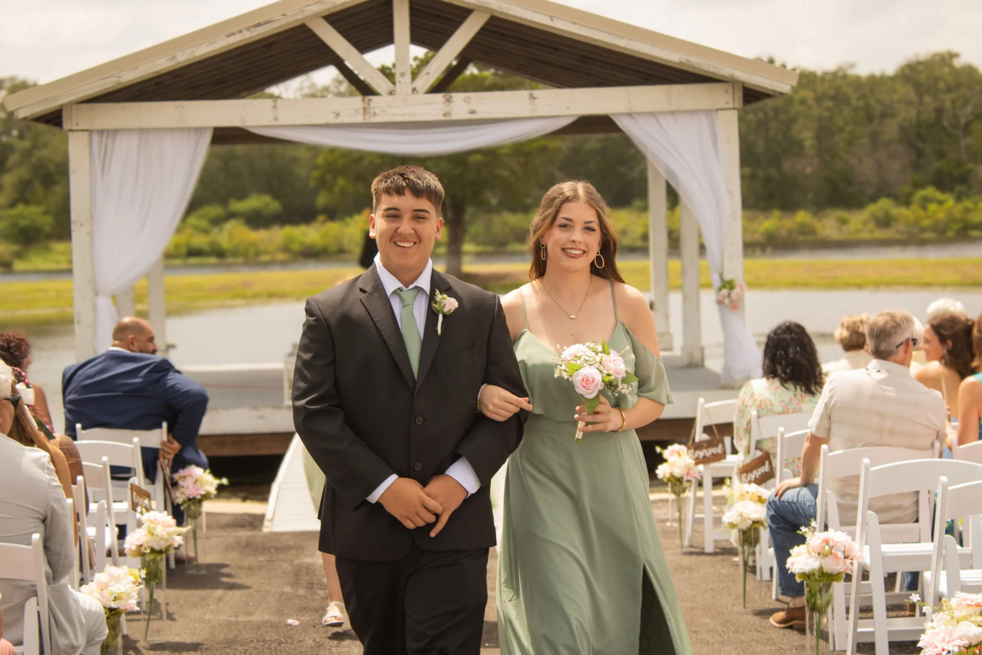 Groomsman escorting a bridesmaid up the aisle after the ceremony at the lakeside pavilion