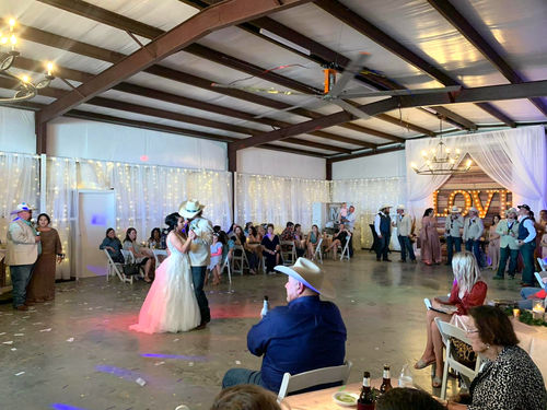 Bride and groom sharing their first dance in the barn as guests look on