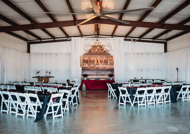 Wide view of the reception hall set with white chairs, black linens and the LOVE marquee head table