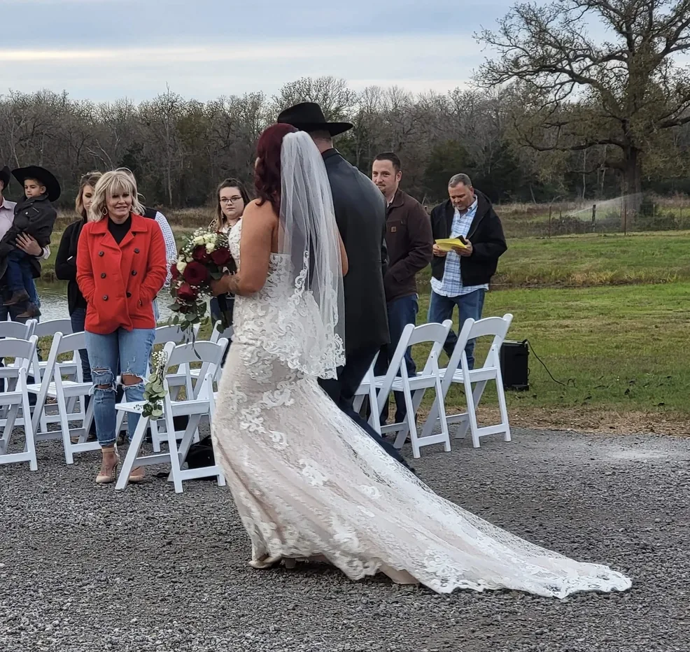 Bride in a lace fit-and-flare gown with a long train walking the gravel aisle toward the lakeside ceremony in Normangee, Texas