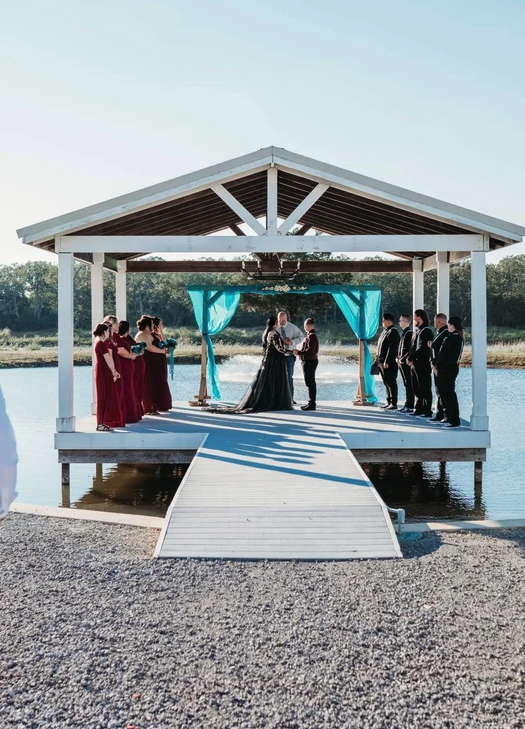 Wide view of the lakeside pavilion ceremony with the wedding party lining the dock
