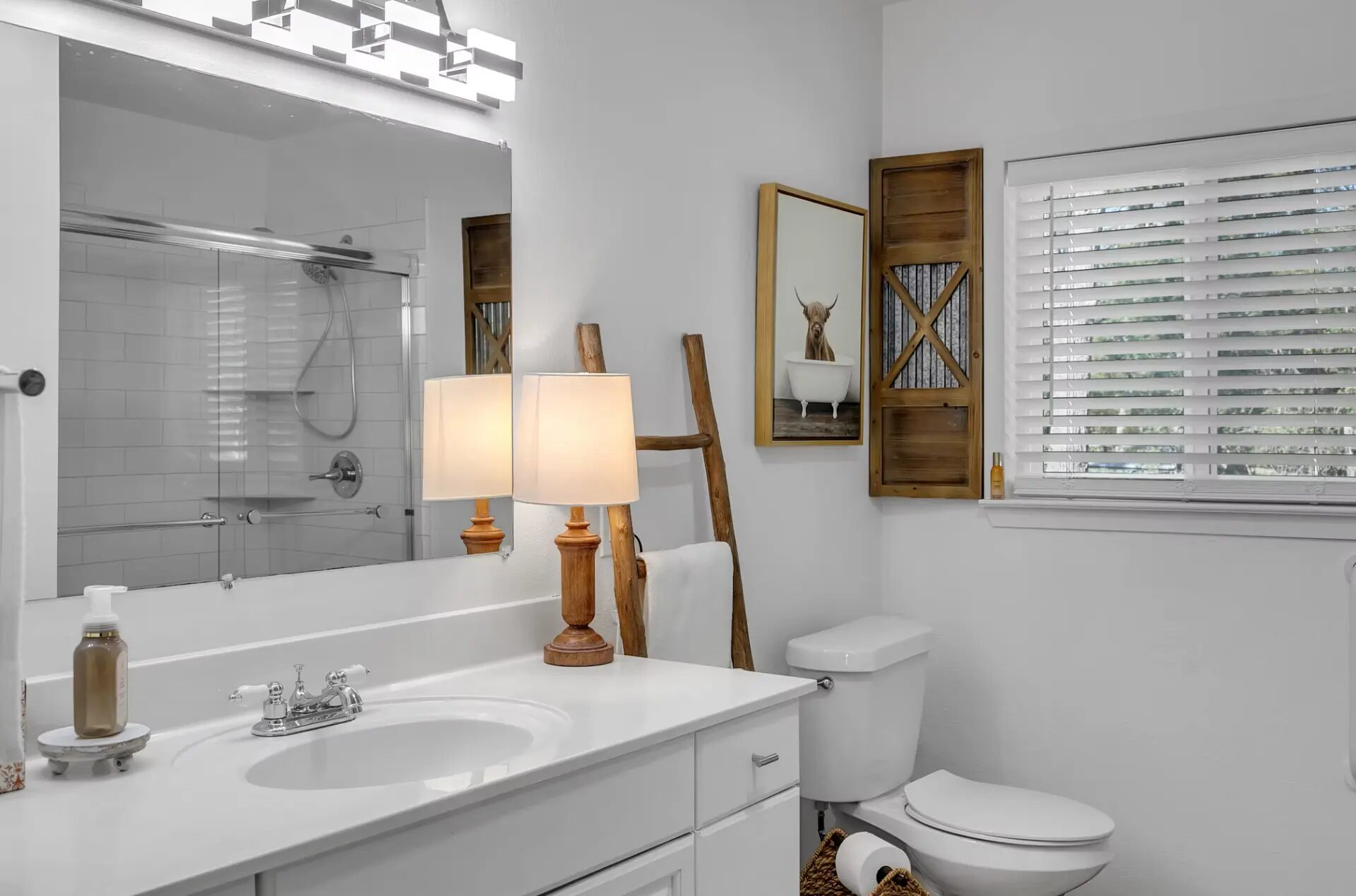 Farmhouse bathroom with a large mirror, glass shower and highland cow art at Reverie at Diamond D