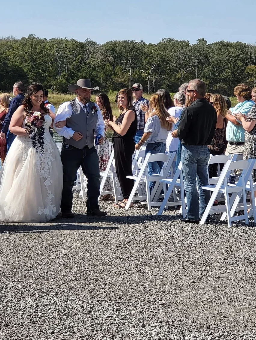 Bride walking down the outdoor aisle on her escort's arm as guests stand at Reverie at Diamond D in Normangee, Texas