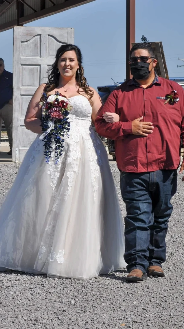 Emily walking toward the outdoor ceremony with her escort while carrying a burgundy and navy cascading bouquet